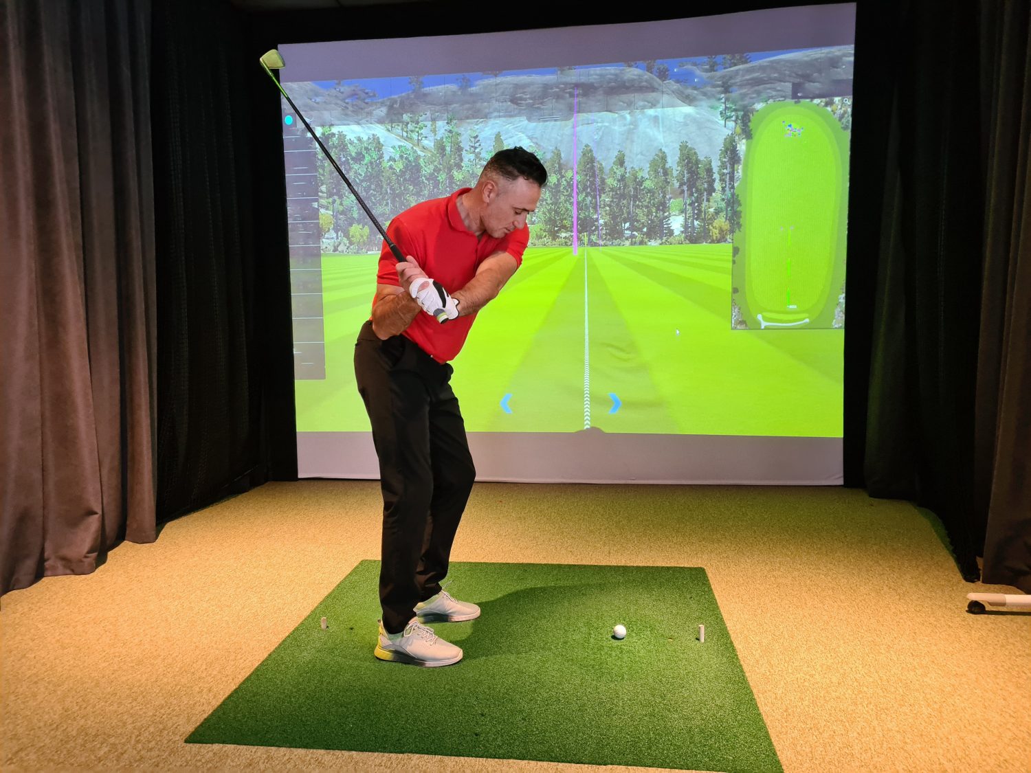 Professional male golfer holding club playing golf indoors on golf simulator