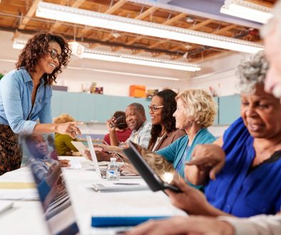 Group Of Retired Seniors Attending IT Class In Community Centre With Teacher A group of older adults engages in a technology class at a community center, using laptops and tablets while a friendly instructor provides guidance. This scene highlights how community center software can streamline class scheduling, making it easier for centers to offer impactful learning experiences.