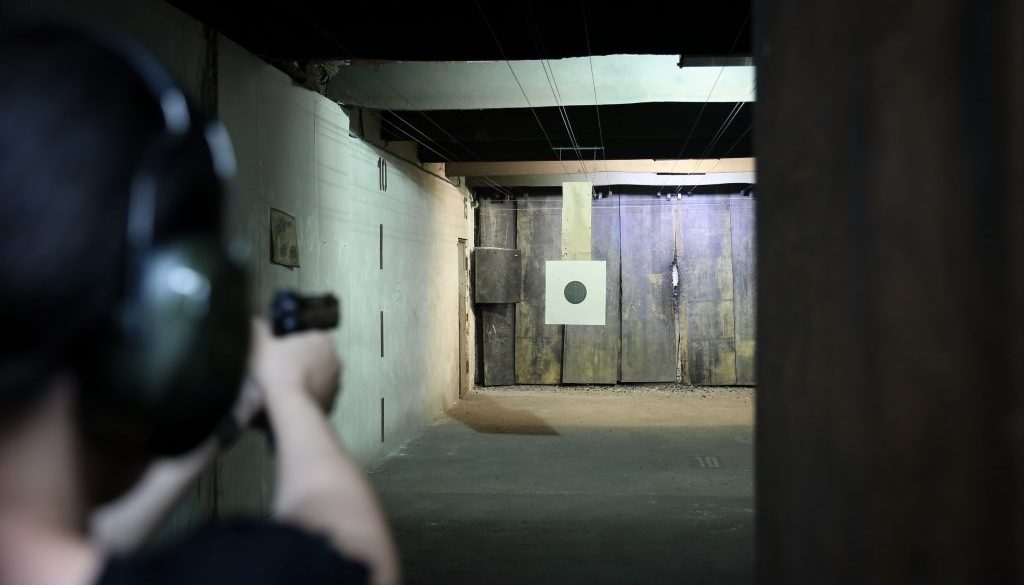 Person aiming at a target in an indoor shooting range, highlighting the need for efficient gun club membership software to manage member access, scheduling, and perks seamlessly.