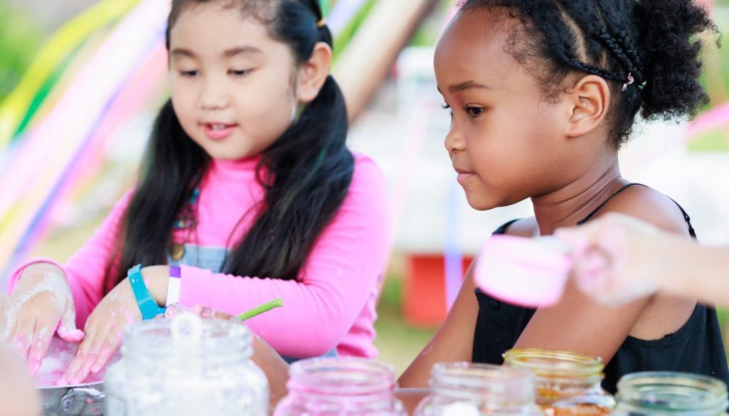 Two young girls engaged in a creative activity with jars of colorful materials at a summer camp, highlighting the fun and variety of programs that can be organized and managed efficiently with summer camp registration software.