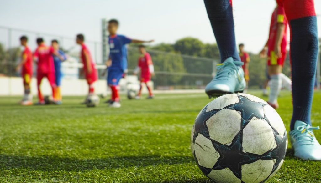 Youth soccer players practicing on a field with a close-up of a soccer ball in the foreground, representing organized training sessions managed efficiently with soccer club management software.
