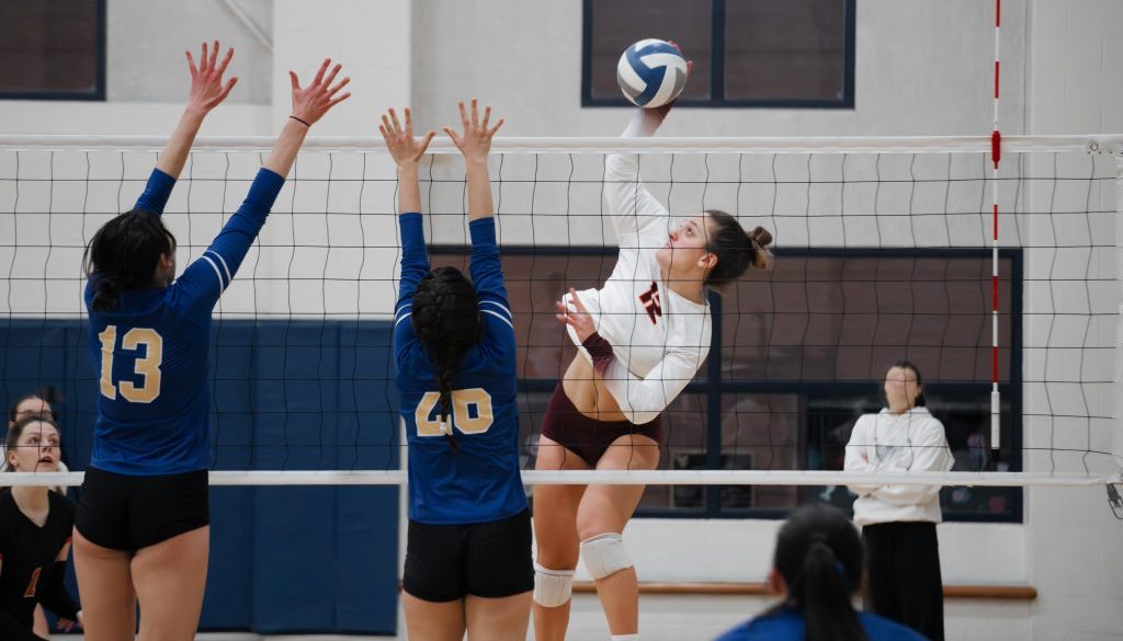 Volleyball outside hitter against a double block Female volleyball players in action at the net during a game, highlighting the need for organized scheduling and payments through volleyball club management software.