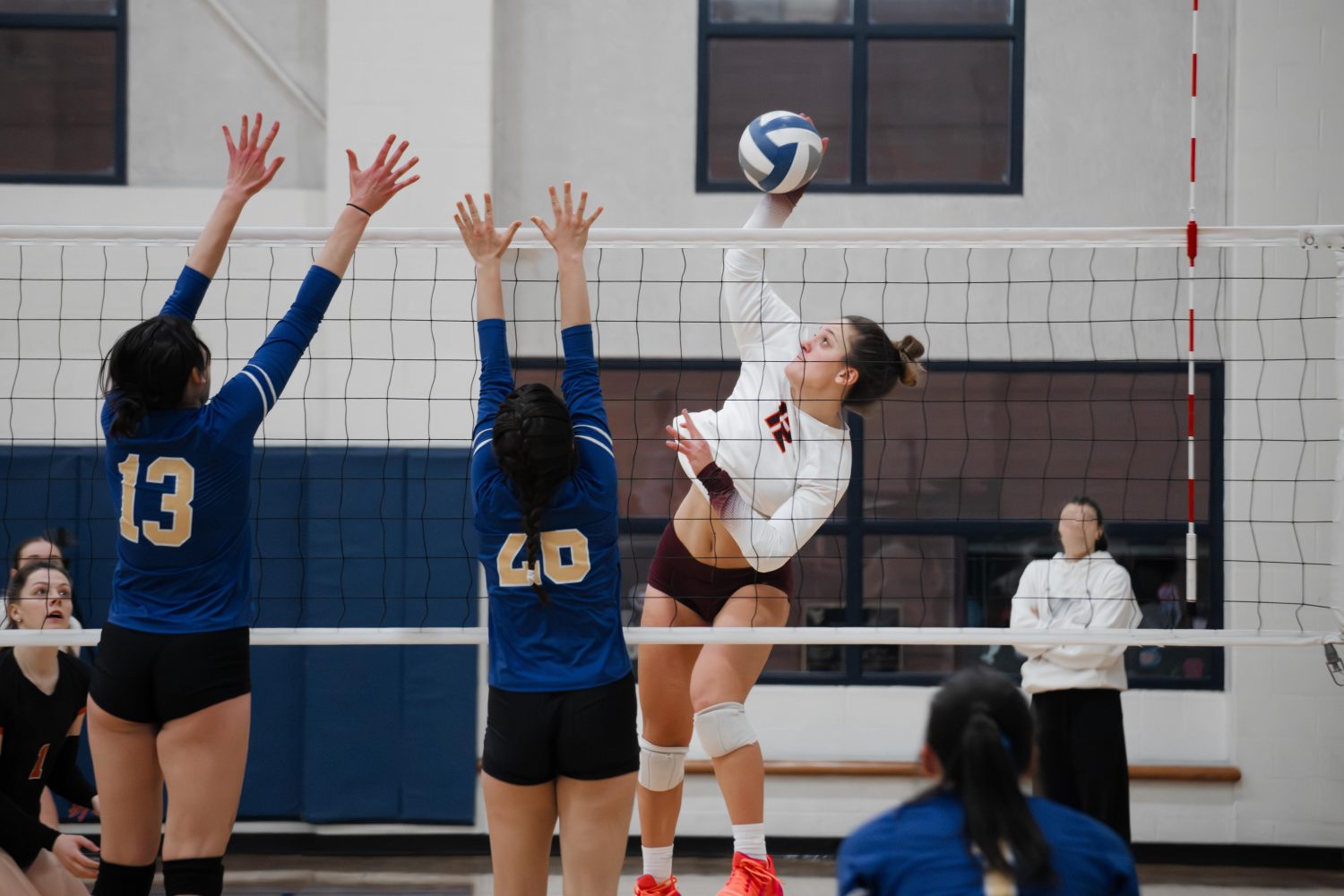 Volleyball outside hitter against a double block Female volleyball players in action at the net during a game, highlighting the need for organized scheduling and payments through volleyball club management software.