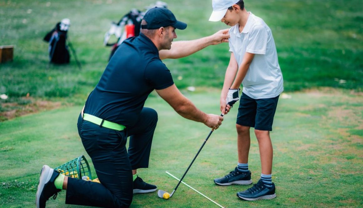 Golf instructor teaching a young student during a private lesson, showcasing the need for flexible scheduling on the go with golf lesson booking software.