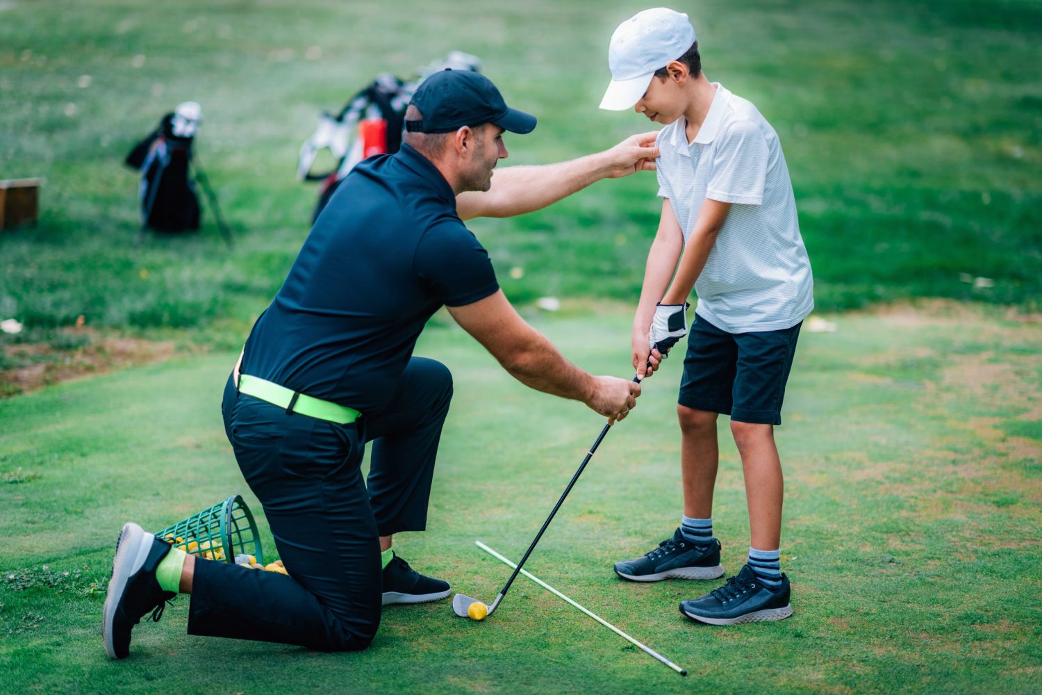 Golf instructor teaching a young student during a private lesson, showcasing the need for flexible scheduling on the go with golf lesson booking software.