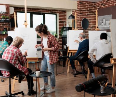 Young teacher helping senior woman to develop illustration technique Senior woman attending an art class at a local community center - an example of programming managed through community center management systems.
