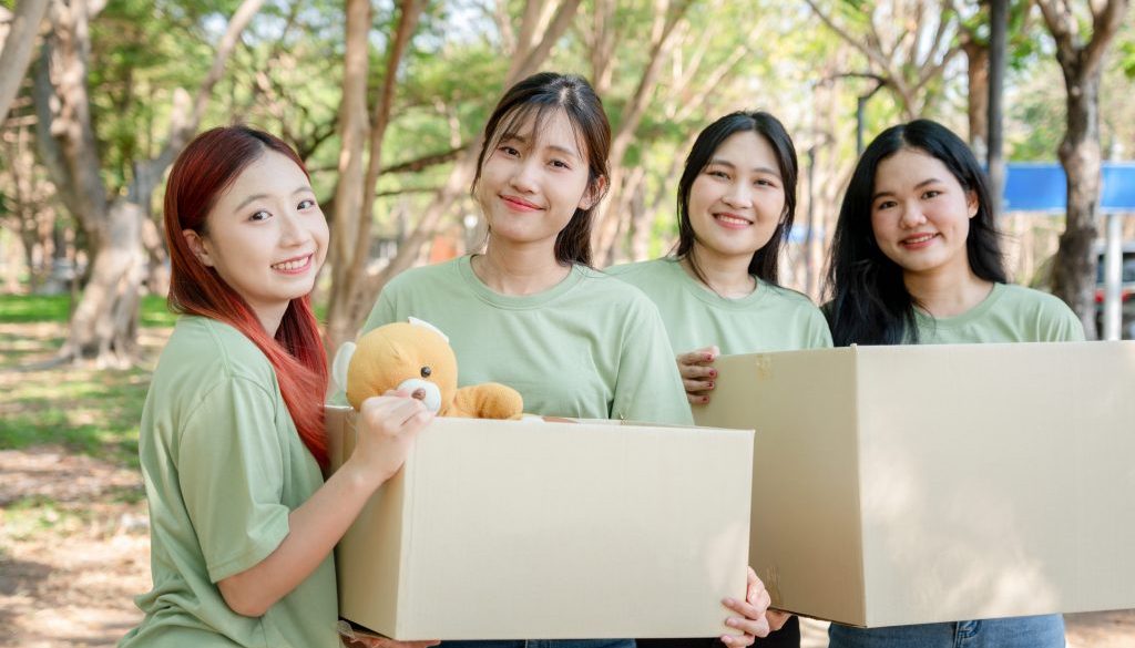 Young Women Volunteers Carrying Donation Boxes Outdoors, Group of Friends Preparing for a Charity Drive