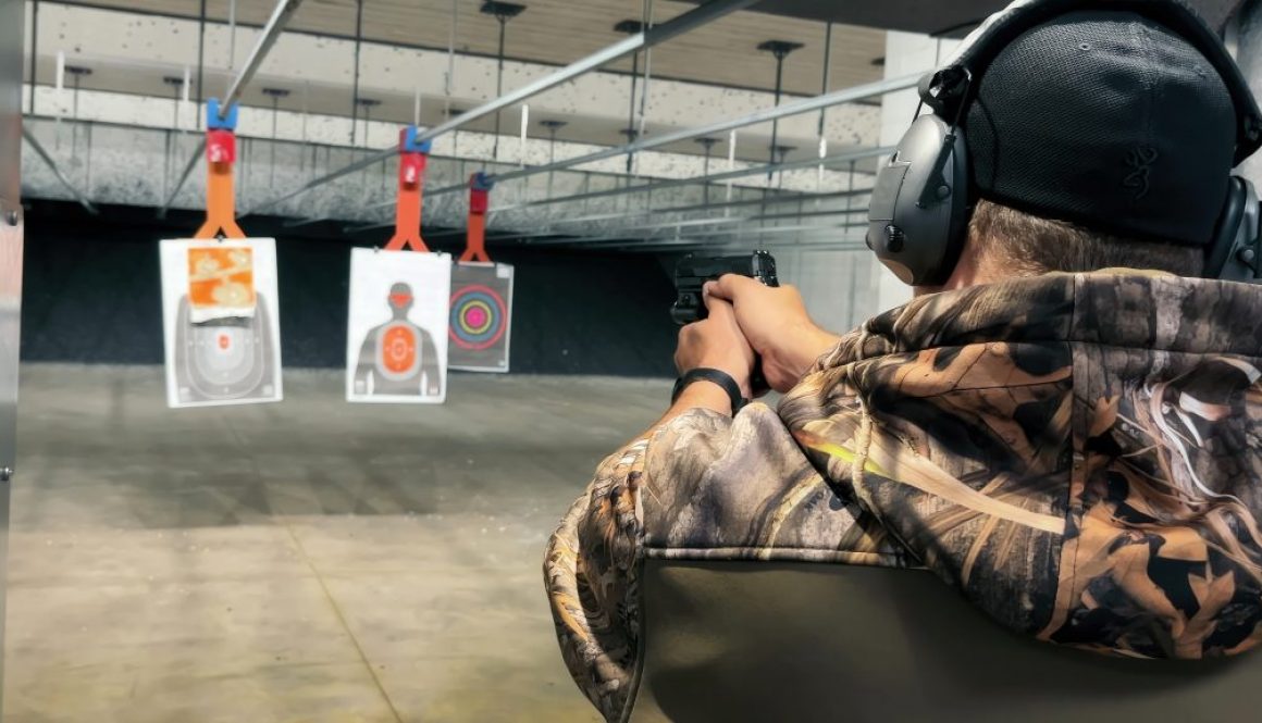 Shooting Practice at Indoor Gun Range. A person wearing camouflage and protective gear takes aim at paper targets during shooting practice at an indoor gun range.