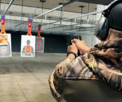 Shooting Practice at Indoor Gun Range. A person wearing camouflage and protective gear takes aim at paper targets during shooting practice at an indoor gun range.
