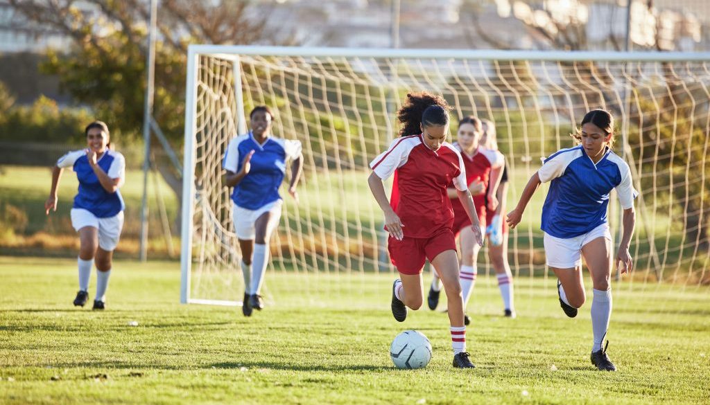 Sports team, girl soccer and kick ball on field in a tournament. Football, competition and athletic female teen group play game on grass. Fit adolescents compete to win match at school championship.