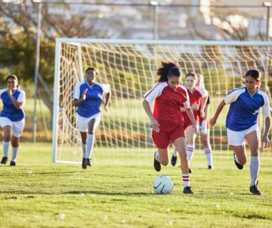 Sports team, girl soccer and kick ball on field in a tournament. Football, competition and athletic female teen group play game on grass. Fit adolescents compete to win match at school championship.